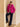 Model wearing the Glow Pink cashmere bomber jacket with fur collar, resting one foot on a step, styled with dark denim and black boots.