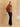 Full-length three-quarter side view of the Warm Camel cashmere bomber jacket with fur collar, paired with dark denim and brown boots.
