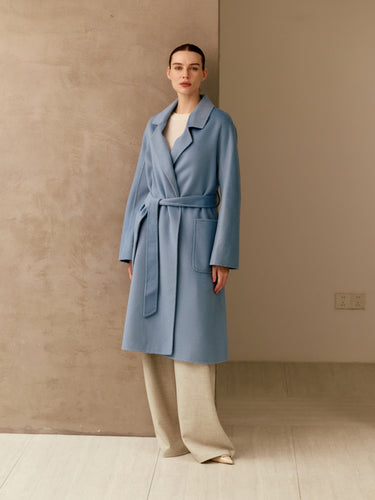 Full-length front view of the Classic Cashmere Wrap Coat in Powder Blue, belted over ivory wide-leg trousers.