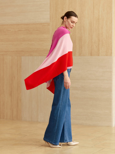 Full-length side view of the Rose Multi cashmere topper, showing bright pink, pale pink and red panels flowing over blue wide-leg denim.