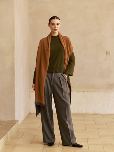 Model wearing the Olive and Deep Chestnut colorblock cashmere travel wrap over an olive sweater with grey wide-leg trousers.