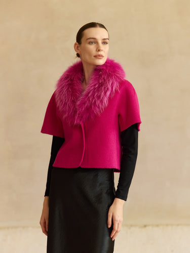 Front view of the Glow Pink short-sleeve cashmere jacket with matching fur collar, worn over a black top and satin skirt.