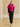 Model walking in the Glow Pink cashmere jacket with fur collar, styled with a black satin midi skirt and heeled sandals.