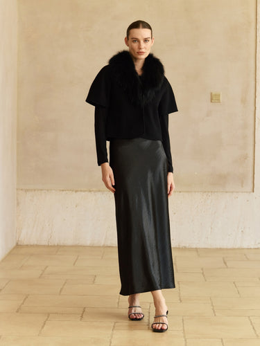 Full-length front view of the Jet Black short-sleeve cashmere jacket with fur collar, layered over a black long-sleeve top and satin midi skirt.