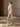 Full-length side view of the Soft Ecru Signature Cashmere Wrap Coat with white fur collar, worn open over neutral trousers.