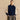 Model wearing a navy and cream speckled layer draped over a navy crewneck sweater and gray pleated trousers.