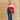 Model wearing a fuchsia, pale pink, and red colorblock topper with an asymmetrical hem over blue wide-leg jeans.