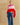 Model wearing a fuchsia, pale pink, and red colorblock topper with an asymmetrical hem over blue wide-leg jeans.