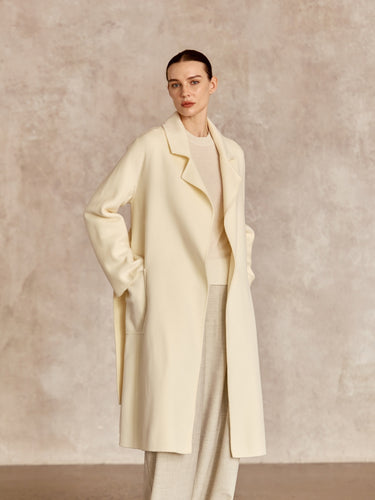 Closer front view of the Classic Cashmere Wrap Coat in Ivory, showing notched lapels and the model’s hand in a side pocket.