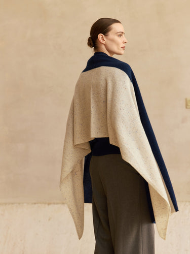 Three-quarter back view of the cashmere travel wrap, showing the flecked Beige Donegal panel across the shoulders and Midnight Navy border.