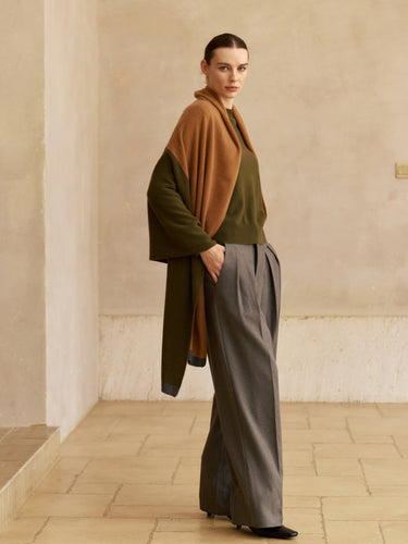 Model wearing the Olive and Deep Chestnut colorblock cashmere travel wrap over an olive sweater with grey wide-leg trousers.