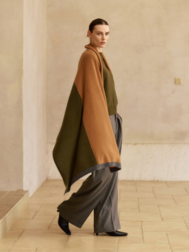 Model walking with the Olive and Deep Chestnut cashmere travel wrap draped over the shoulders, showing its long panels and contrast trim.