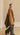 Model walking with a camel and olive color block wrap with gray trim draped over an olive sweater and gray trousers.