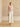 Full-length front view of the Blush short-sleeve cashmere jacket with matching fur collar, styled with an ivory midi skirt and heels.