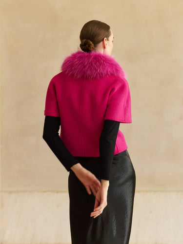 Back view of the Glow Pink short-sleeve cashmere jacket, showing the fur collar and compact silhouette over a black top.