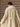Closer back view of the Soft Ecru Signature Cashmere Wrap Coat, showing the white fur collar, belt across the waist and long sleeves.