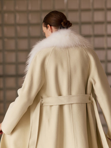 Closer back view of the Soft Ecru Signature Cashmere Wrap Coat, showing the white fur collar, belt across the waist and long sleeves.